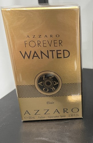 A boxed fragrance product labeled Azzaro Forever Wanted Elixir, shown in a metallic gold box on a dark tabletop against a light wall.
