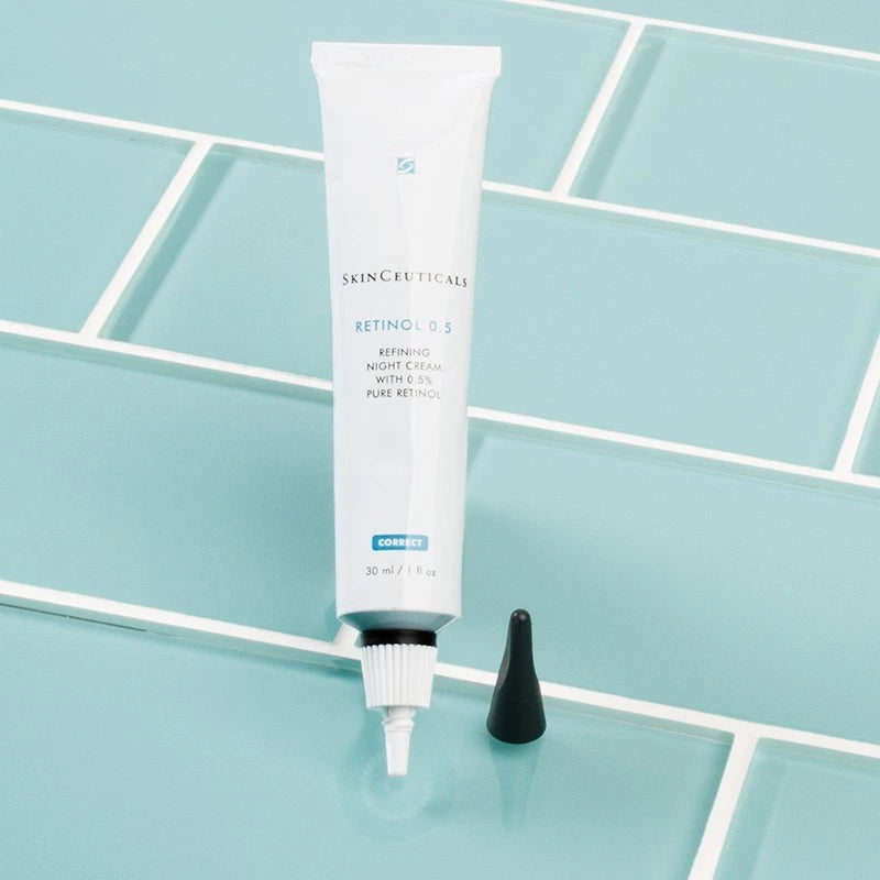 A tube of Skinceuticals Retinol 5 Retinoid Night Cream with its black applicator cap placed beside it on a glossy light blue-green tiled surface.