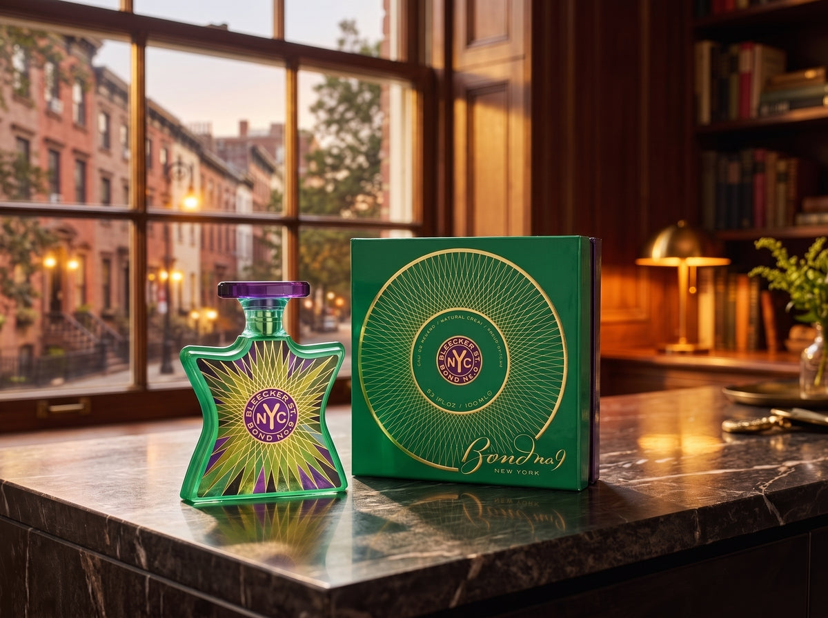 A green and purple Bvlgari Bonita perfume bottle stands next to its green presentation box on a polished dark marble countertop, with a warm, softly lit interior room and window in the background.