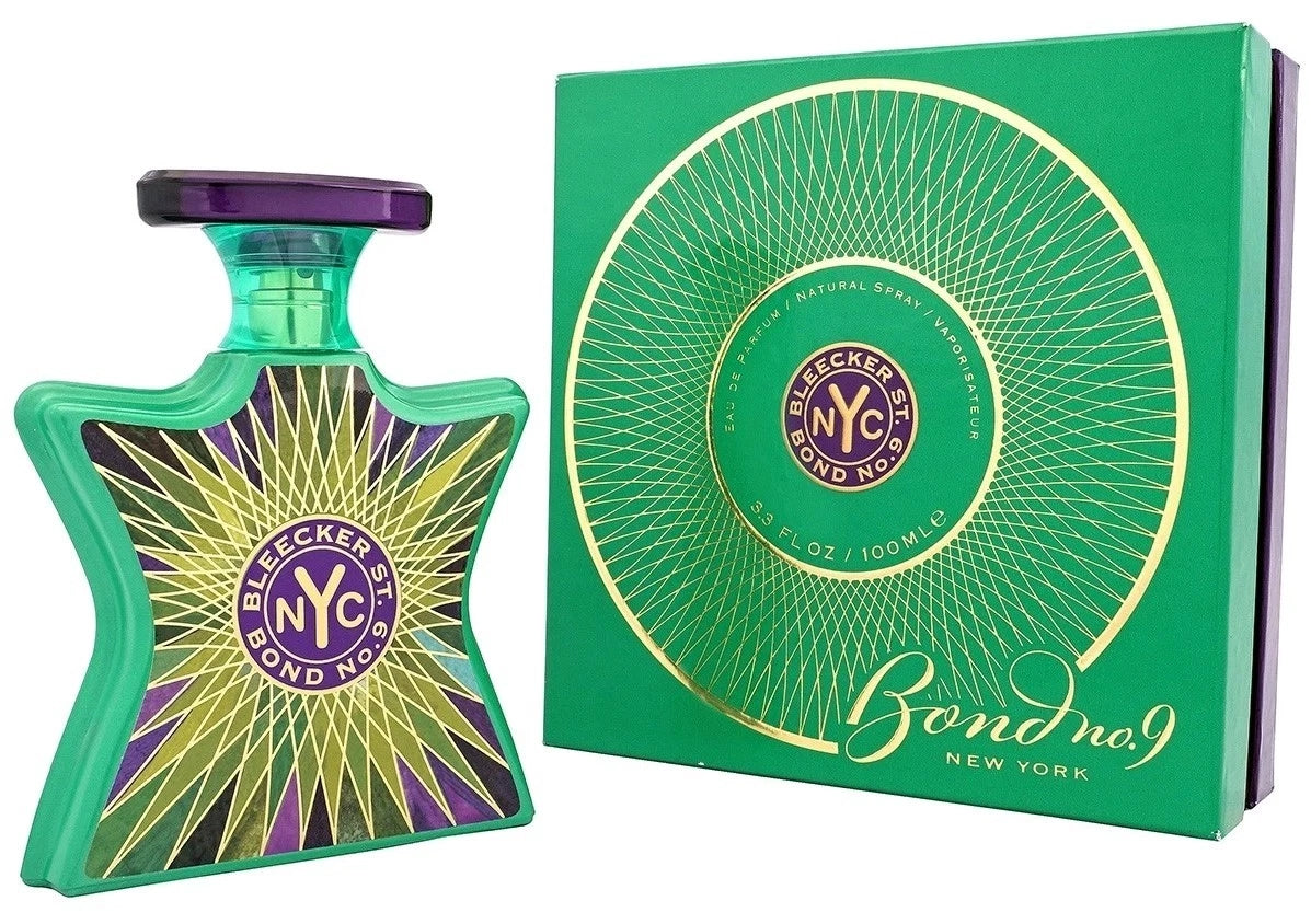 Bond No. 9 New York fragrance bottle in a distinctive star shape with a green body, purple cap, and yellow/gold geometric pattern, shown next to its green gift box with gold circular detailing.