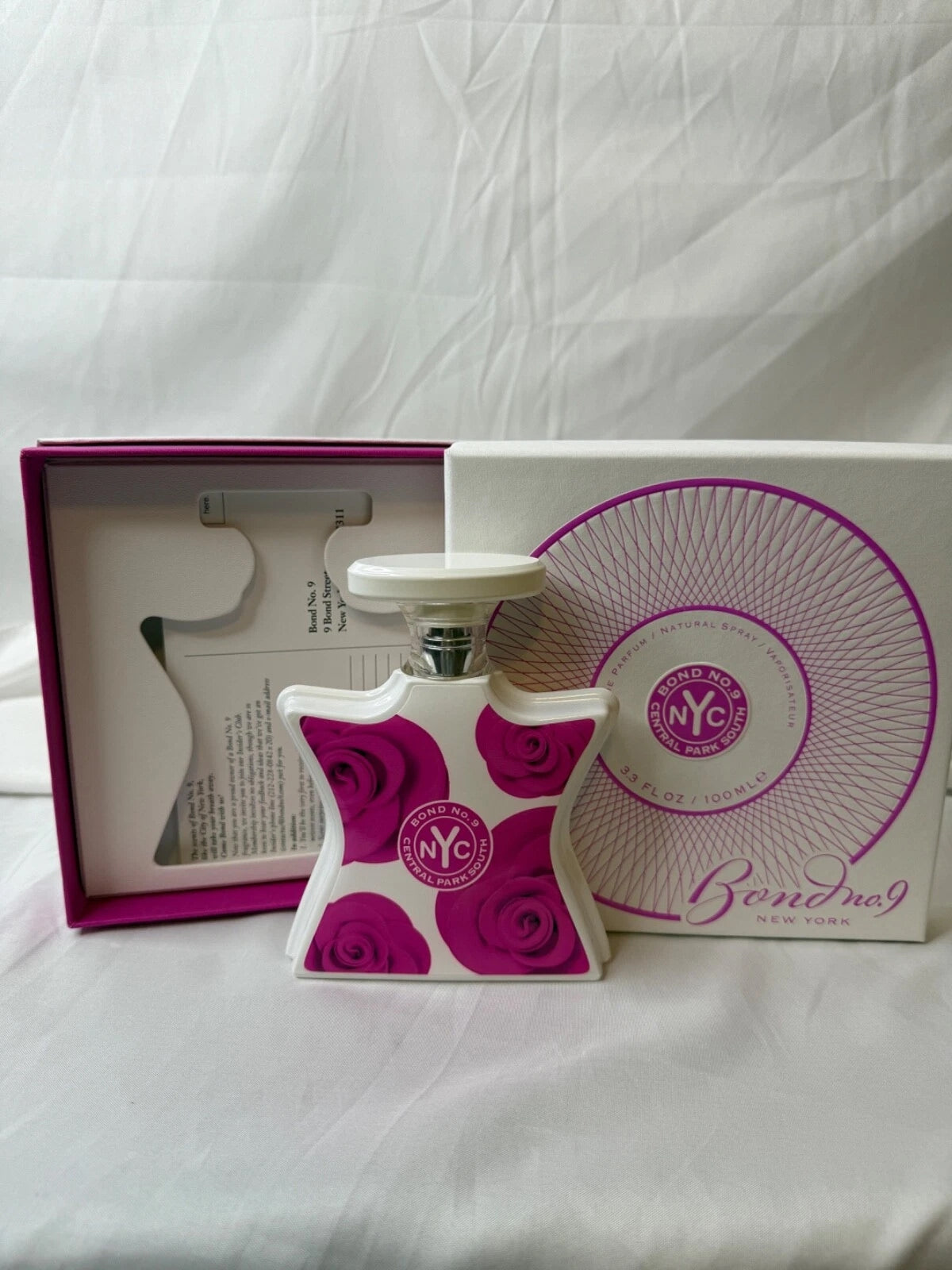 Bondnet NYC perfume bottle with a white and magenta rose pattern, shown next to its white and magenta gift box and inner packaging on a white fabric background.