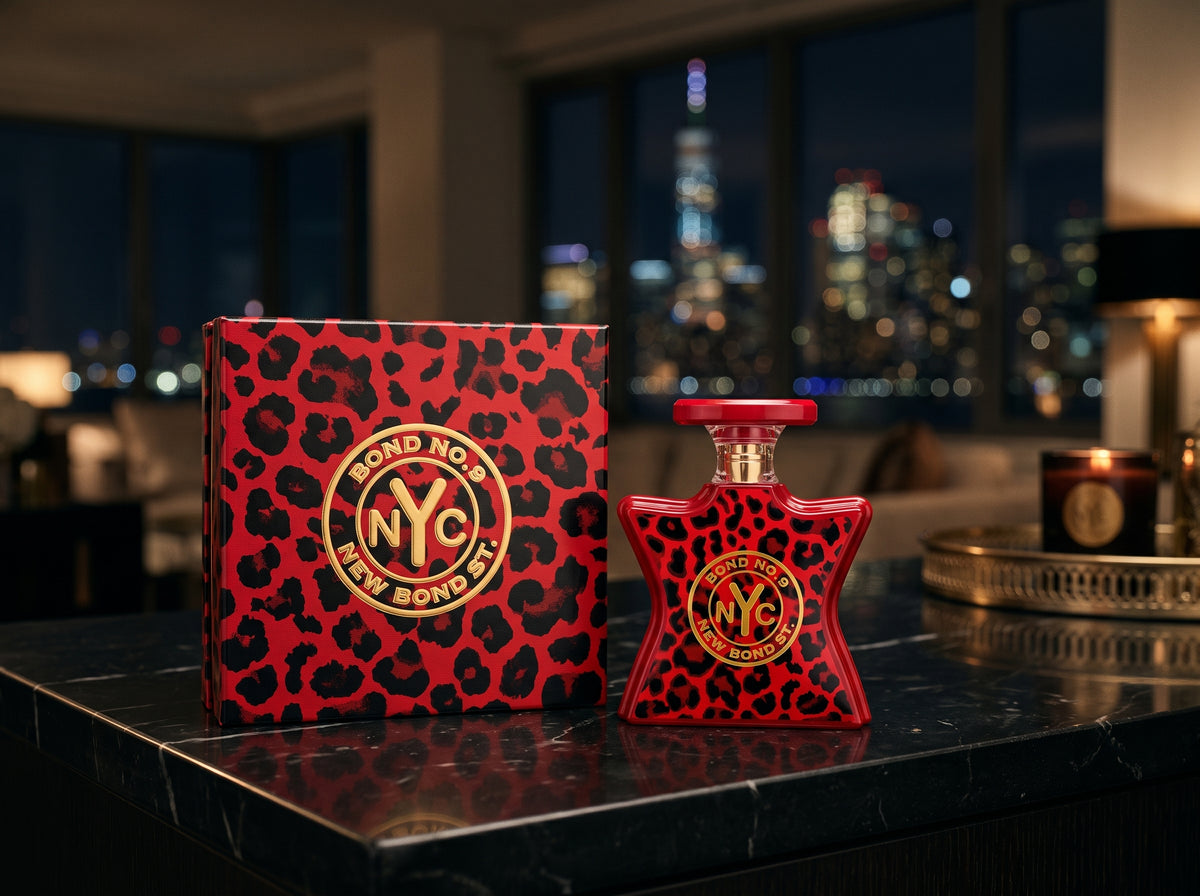 A red and black leopard-print perfume bottle and matching box with gold circular NYC branding, displayed on a dark marble surface in front of a blurred nighttime city skyline.