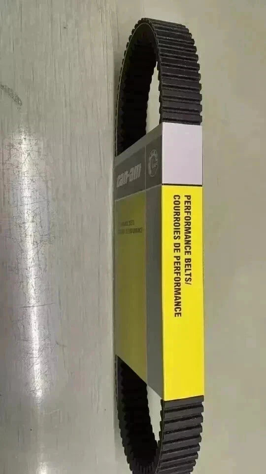 A black rubber performance belt with a yellow and gray paper wrap label, standing vertically on a light gray metallic surface.