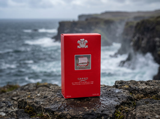 A red rectangular product box with a silver Viking ship emblem and text, standing on dark rocks with a blurred ocean and cliffside background.