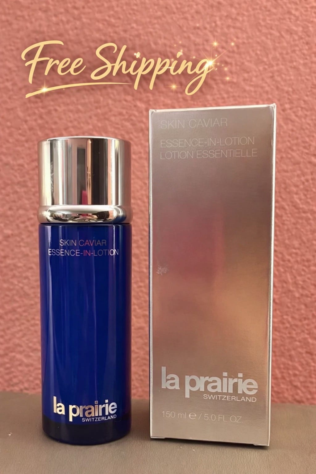 La Prairie Skin Caviar Essence-In-Lotion bottle in deep blue with a silver cap, shown next to its metallic silver box against a textured pink background with a 'Free Shipping' graphic overlay.