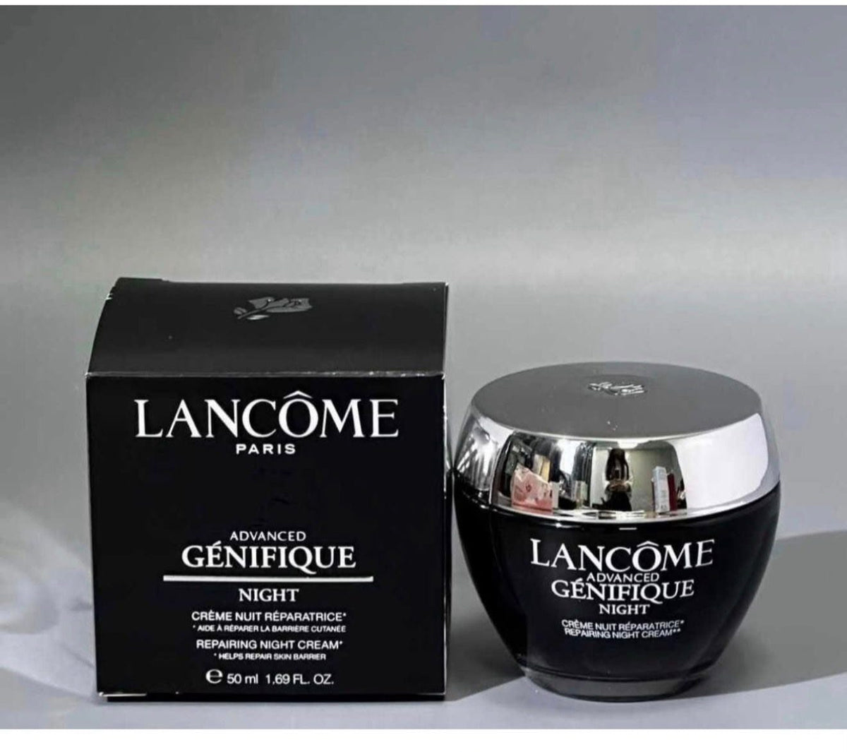 Lancôme Paris Advanced Génifique Night cream shown with its black retail box and matching jar featuring a reflective silver lid, set against a neutral gray background.