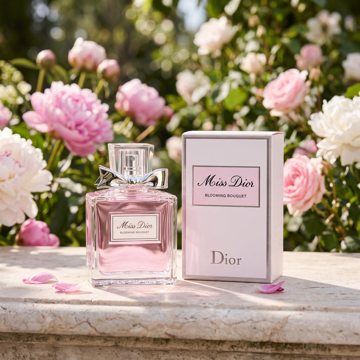 Dior Miss Dior Blooming Bouquet perfume bottle with a pink liquid and silver bow, displayed next to its pink and white box on a stone ledge with pink and white flowers in the background.