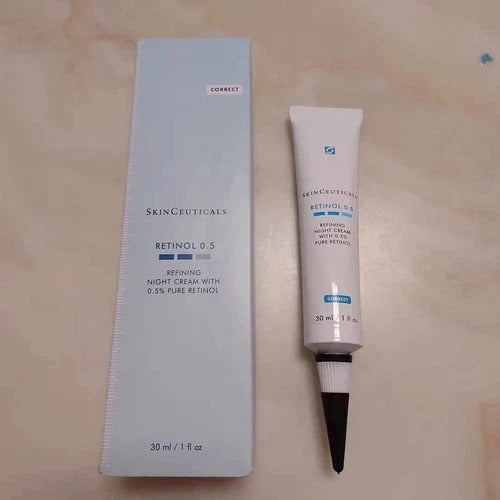 SkinCeuticals Retinol 0.5 Refining Night Cream shown with its light blue outer box and the white squeeze tube with a black applicator tip, placed on a beige surface.
