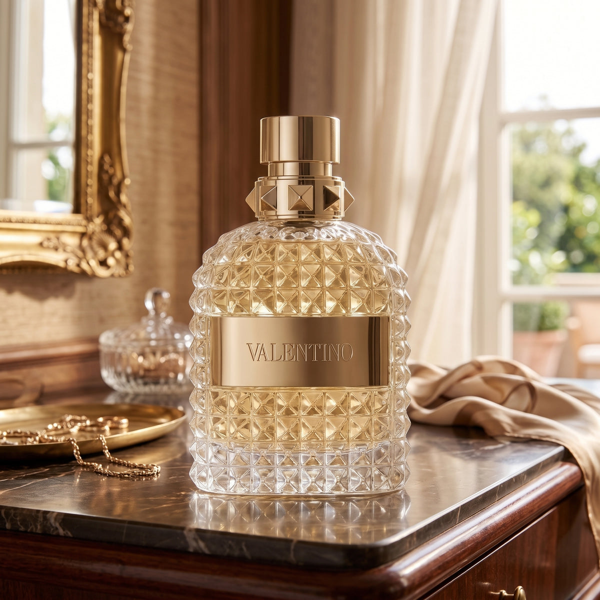 A bottle of Valentino perfume with a textured clear glass body and a shiny gold cap, displayed on a polished wooden dresser in an elegant room.