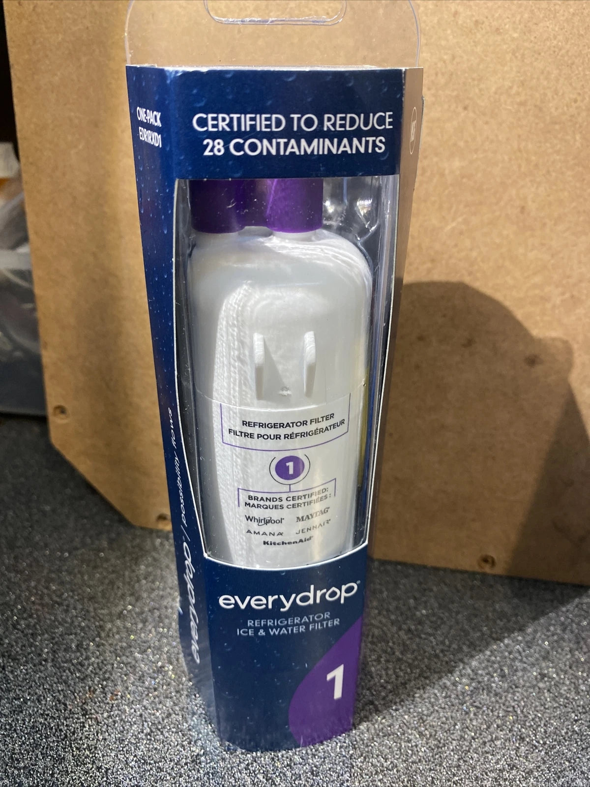 A boxed Everydrop Refrigeration Ice & Water Filter 1 in its original retail packaging, standing upright on a gray carpet in front of a cardboard box.