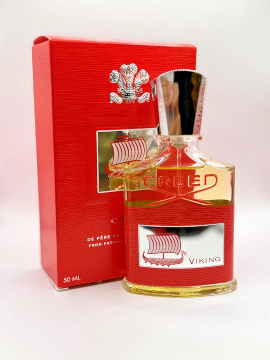 A bottle of Viking De Père Creed fragrance with a red textured label and silver cap, shown next to its matching red box on a light background.