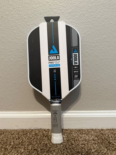 A Joola Pro 10.5 pickleball paddle leaning against a beige wall on a carpeted floor.