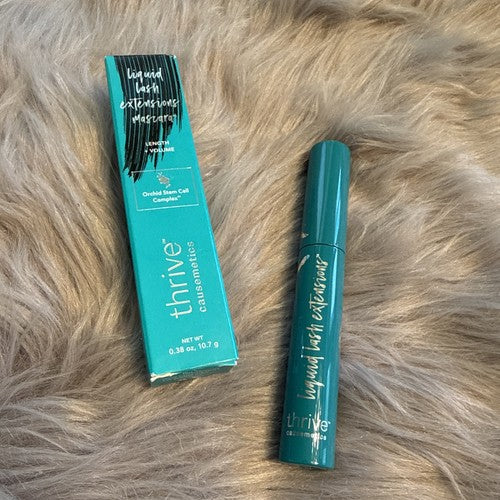 Thrive Cosmeceuticals Liquid Last Extensions Mascara shown in its teal tube next to its matching teal box, placed on a beige faux fur surface.