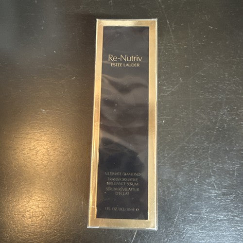 Estel Lauder Re-Nutriv Ultimate Radiance Serum in its original gold and black packaging, placed on a dark, scratched surface.